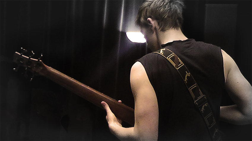 A man playing a bass guitar wearing a sleevless shirt.